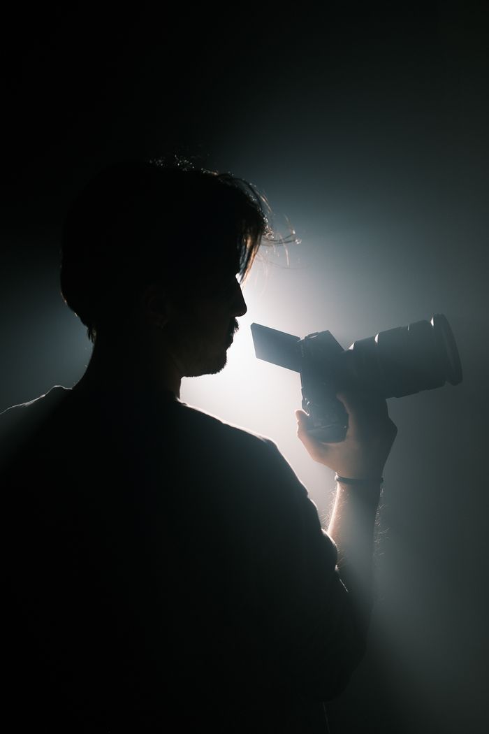 Silhouette of a photographer holding a camera in dramatic lighting.